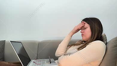 Laptop work pauses as woman on sofa holds head with