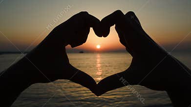 Sunset over sea in heart made of hands