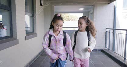 African American child girls holding hands walking to class after friend tapping shoulder backpacks