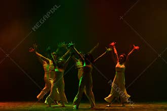 Synchronized Contemporary Dancers Raising Arms Beneath Colorful Stage Lights