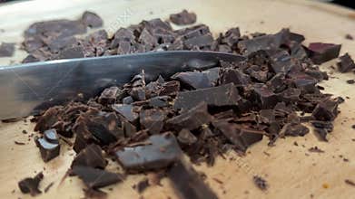 Real dark chocolate finely chopped by hand on rustic wooden board for artisan chocolate baking and homemade
