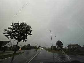Rainy suburban road seen through wet windshield with raindrops, glowing
