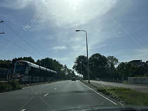 Sunny urban road with modern tram on side track, empty lane, tall