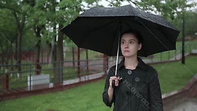 Lonely sad woman walks down the street in heavy rain. Slow motion