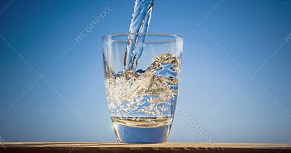 Blue water is flowing into the glass forming bubbles and splashes