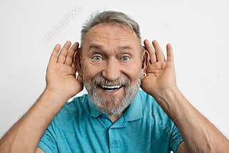 An elderly man with toothy smile having fun and holding hands near his ears and asking what did you say .Hearing problems