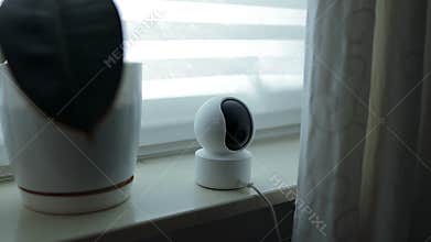 Home security camera or baby monitor standing on a windowsill.