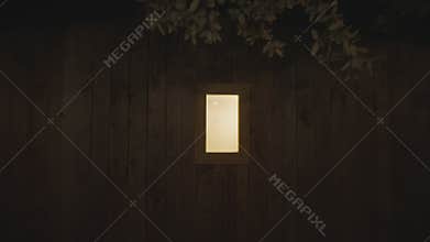 Camera pulling back from a glowing window on a wooden cabin wall at night