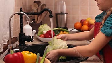 Little girl washing vegetables at the kitchen sink