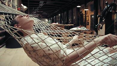 Woman with short hair wearing glasses relaxing on the hammock in her loft apartment