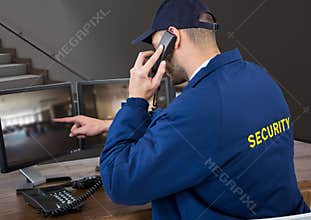 Security guard in his office phoning and pointing something in the screen