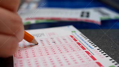 Woman hands filling lucky number on 649 lottery ticket.