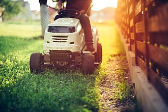 Details of landscaping and gardening. Worker riding industrial lawnmower