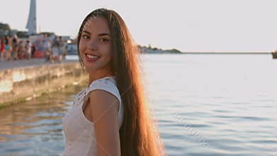 Stunning brunette with long hair dressed in the white tight dress standing by the sea