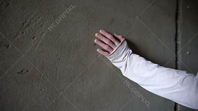 Hand touches and slides on a concrete wall with cracks