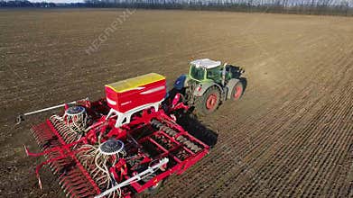 The tractor pulls a large seeder across the field. Sowing campaign in early spring, rural landscape. Concept - modern