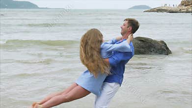Close up man is circling a girl in his arms on a sea sandy beach. A pair of lovers swirl in slow motion