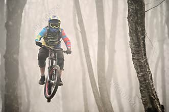 A mountain bike rider jumps from a springboard in a foggy forest, in the Caucasus Mountains