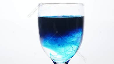 Blue ink dropping into a glass of water on a white background. The poison in the glass concept.