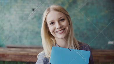 Portrait of young caucasian blonde woman looking at camera and smiling at modern office. Successful employee at work.