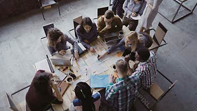Top view of mixed race business team sitting at the table at loft office and working. Woman manager brings the document.