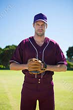 Portrait of confident baseball pitcher standing against sky