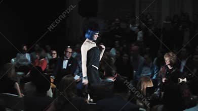 Model in black dress blue hair wig catwalking at fashion runway show