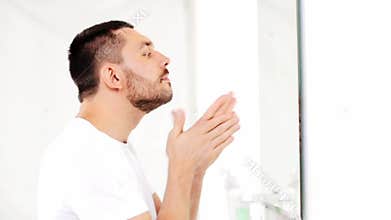 Man applying after shave oil to face at bathroom