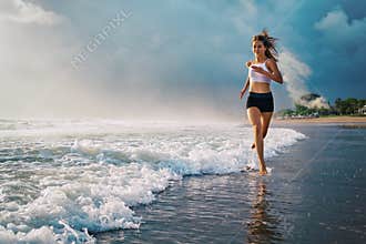 Active sporty woman run along sunset ocean beach. Sports background.
