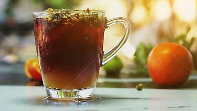 Glass of ice tea with сhrysanthemums and orange, ice cubes on dark wooden table