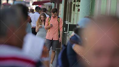 Young couple walk along the busy city street and look at their smartphones in slow motion