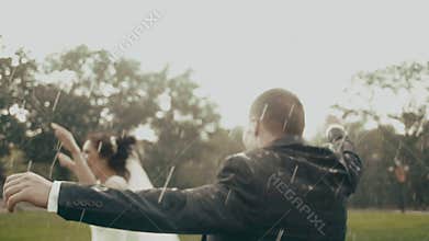 The happy newlyweds are dancing in the rain in the park during the summer.