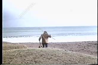 Rear view of man walking down beach with fishing rods
