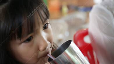 Young Asian child drinking a glass of water .