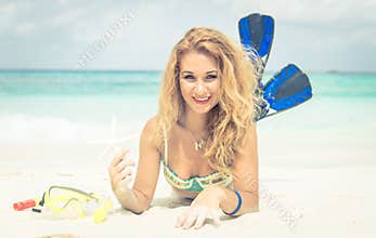 Woman lying on the sand holding starfish and wearing fins.