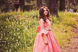 Happy curly child girl in fairytale princess pink dress dancing in summer forest