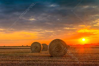 Sunset over farm field with hay bales