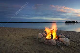 Camp fire on sandy beach, beside lake at sunset. Minnesota, USA