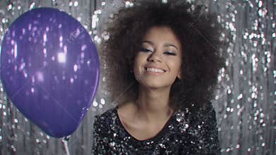 Cute afro american woman with balloon blowing confetti over shiny background.