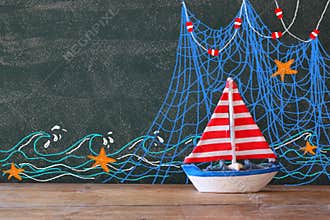 Photo of wooden sailing boat in front of chalkboard with nautical illustrations.