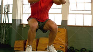 Fit man doing box jumps in gym