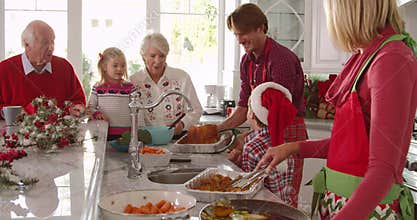 Extended family group prepare Christmas lunch in kitchen - Father takes turkey from oven and bastes it with spoon