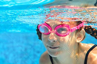 Child swims in pool underwater, happy active girl in goggles has fun in water, kid sport on family vacation