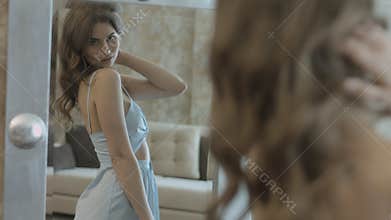 Stylish young woman in the dress twisting in front of the mirror and looking at her reflection