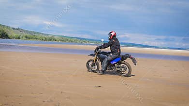 The feeling of freedom and Moto aesthetics. Motorcyclist riding on his bike on sandy beach.