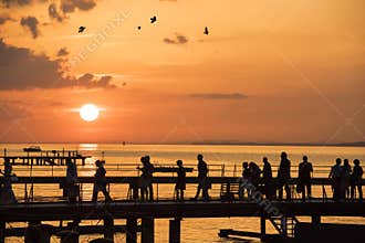 People Walking on Sunset over Bridge, Lake Constance, Bregenz, Austria. Silhouettes of Men, Women, Children in Front of Lake.