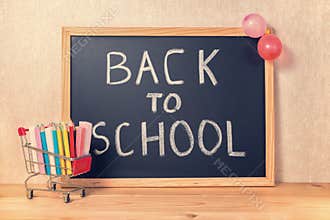 education concept with text back to school is written in chalkboard, shopping cart, pens, colorful chalks and balloons on wooden