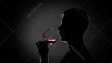 Man drinks cognac from a glass. Grey. Silhouette. Close up. Slow motion