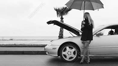 Black and white footage of a woman standing under the umbrella near the broken auto