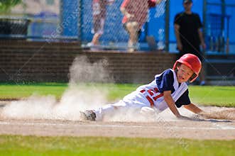 Little league baseball player sliding home.